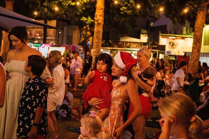 gold-coast-christmas-event Families enjoying a Gold Coast Christmas event outdoors at night, with festive lights, food stalls, and holiday cheer in the warm summer air.